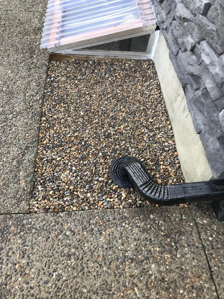 Downspout extension draining onto a gravel strip beside a foundation